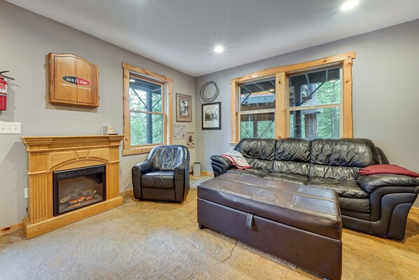 A living room with a fireplace, leather furniture, large windows, and a Jack & Coke sign. - 1 Mi to Cle Elum Lake! Family Cabin w/ Game Room (Ronald)