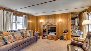 A cozy living room with a leather sofa, wooden panel walls, a television, and a small fan. - Near Grindstone Lake & Family Fun! Cozy Cabin (Ruidoso)