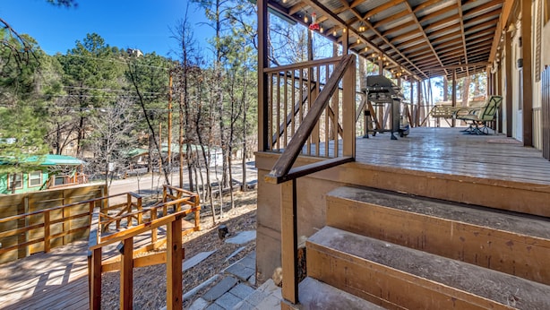 A covered outdoor area with wooden steps leading to a deck, surrounded by trees and a clear sky. - Near Grindstone Lake & Family Fun! Cozy Cabin (Ruidoso)