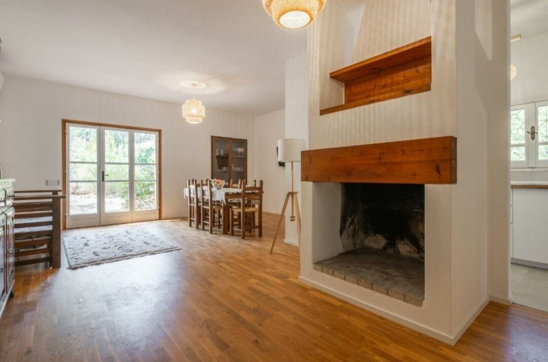 Ein geräumiges Wohnzimmer mit Holzboden, Kamin, Essbereich mit Stühlen und einem großen Fenster.