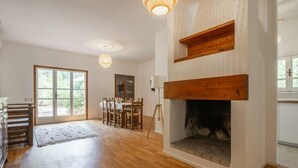 Ein geräumiges Wohnzimmer mit Holzboden, Kamin, Essbereich mit Stühlen und einem großen Fenster.