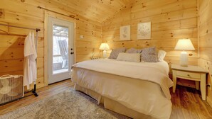 Ett sovrum i en stuga med träpanel, innehållande en säng, två sänglampor, en dörr och ett litet bord.