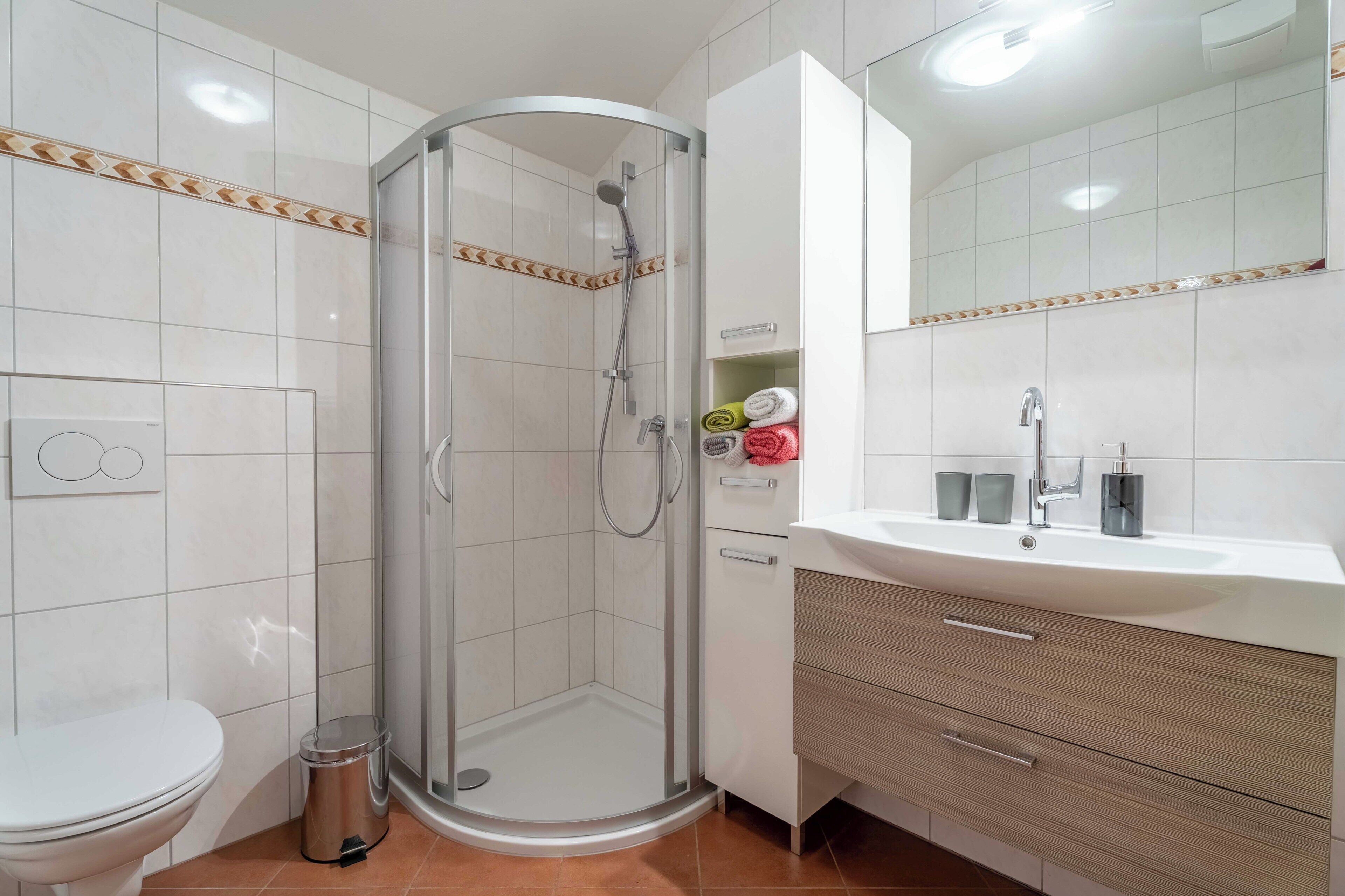 Een badkamer met een douchecabine van glas, toilet, wastafel met spiegel en kast.