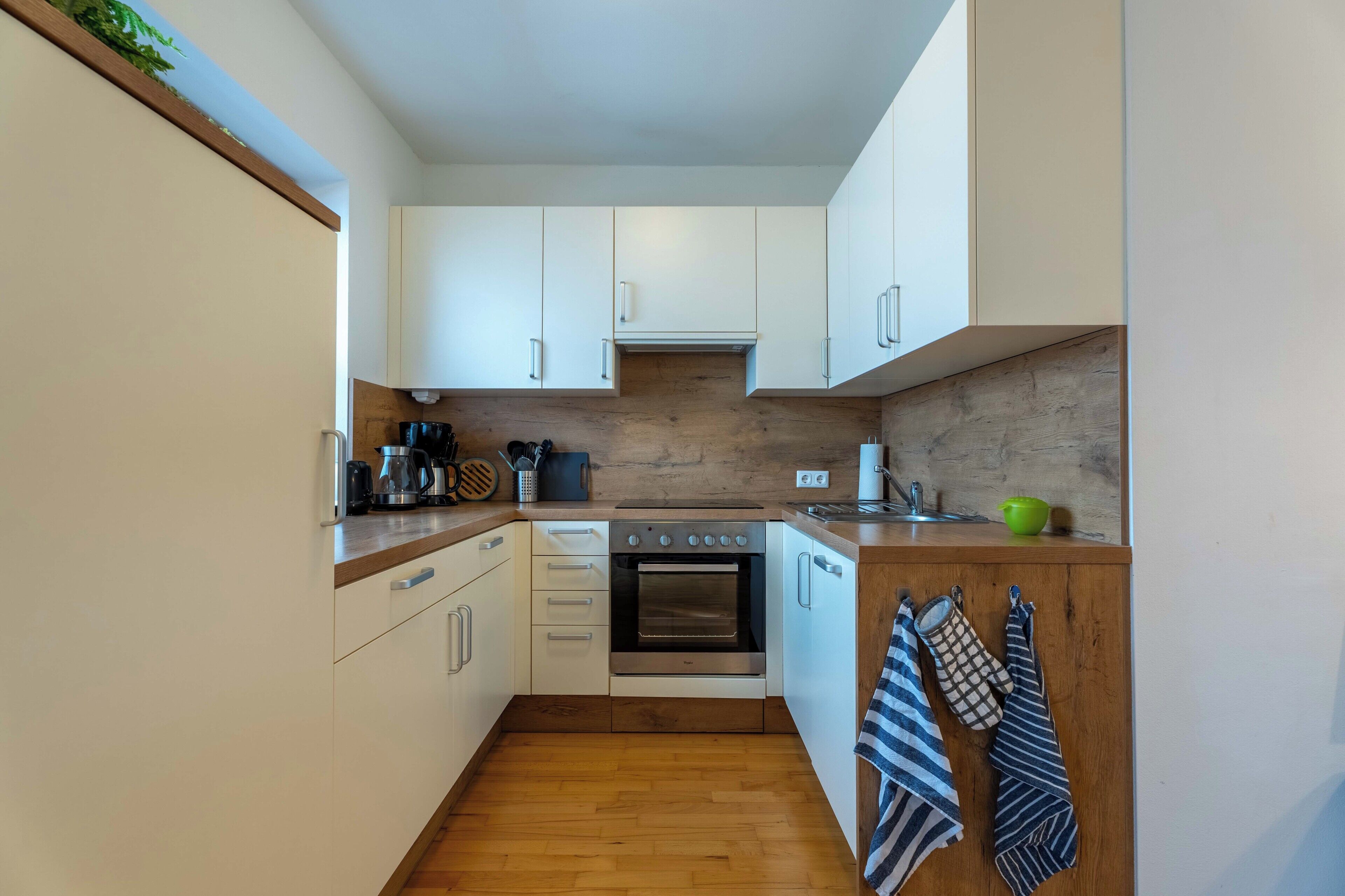 A compact kitchen with white cabinets, a built-in oven, and wooden flooring.