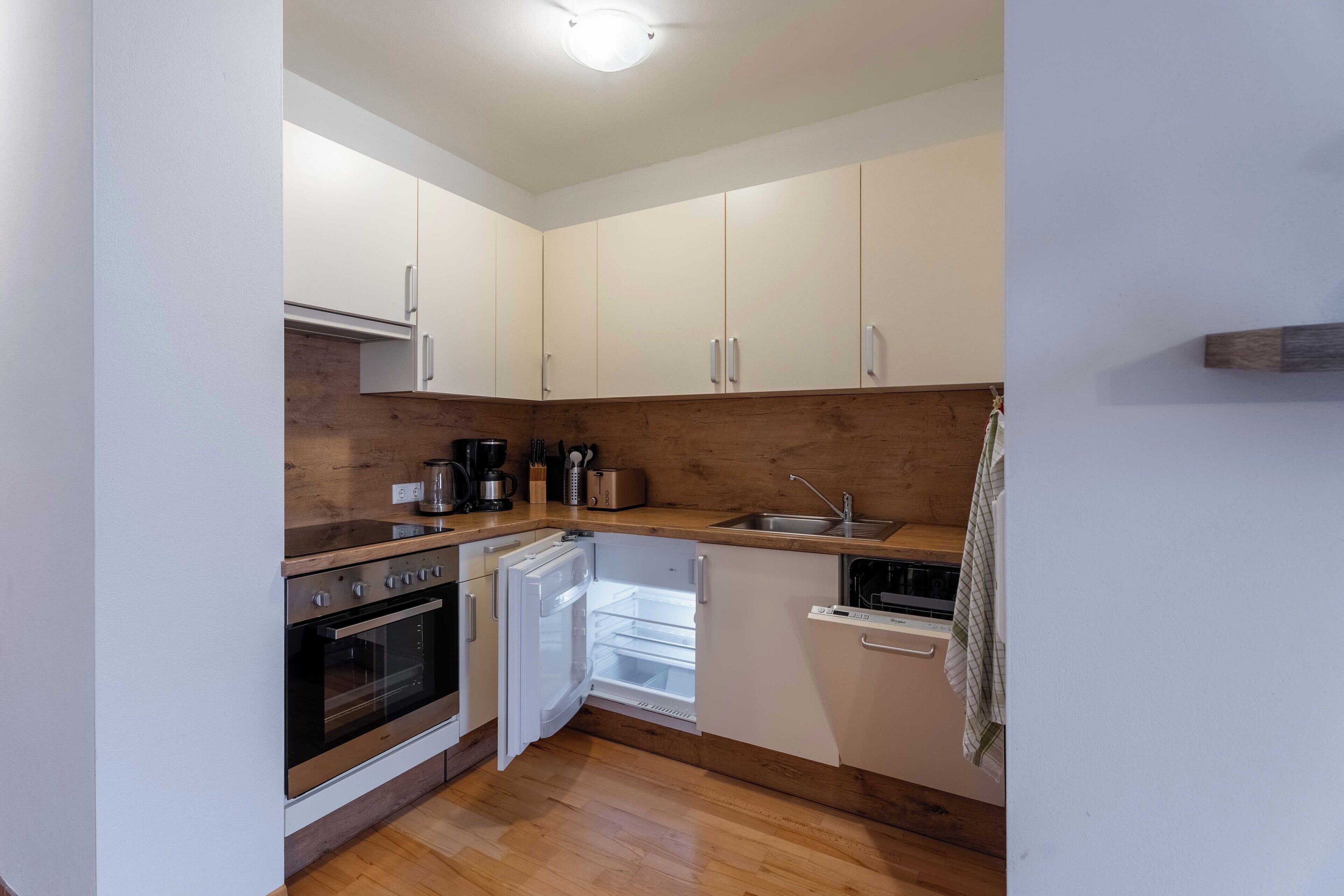 Une cuisine compacte avec des meubles blancs, un four encastré, un lave-vaisselle et un plan de travail en bois.