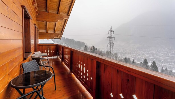 Ein Holzbalkon mit Glastisch und Stühlen, mit Blick auf eine verschneite Landschaft und Stromleitungen.