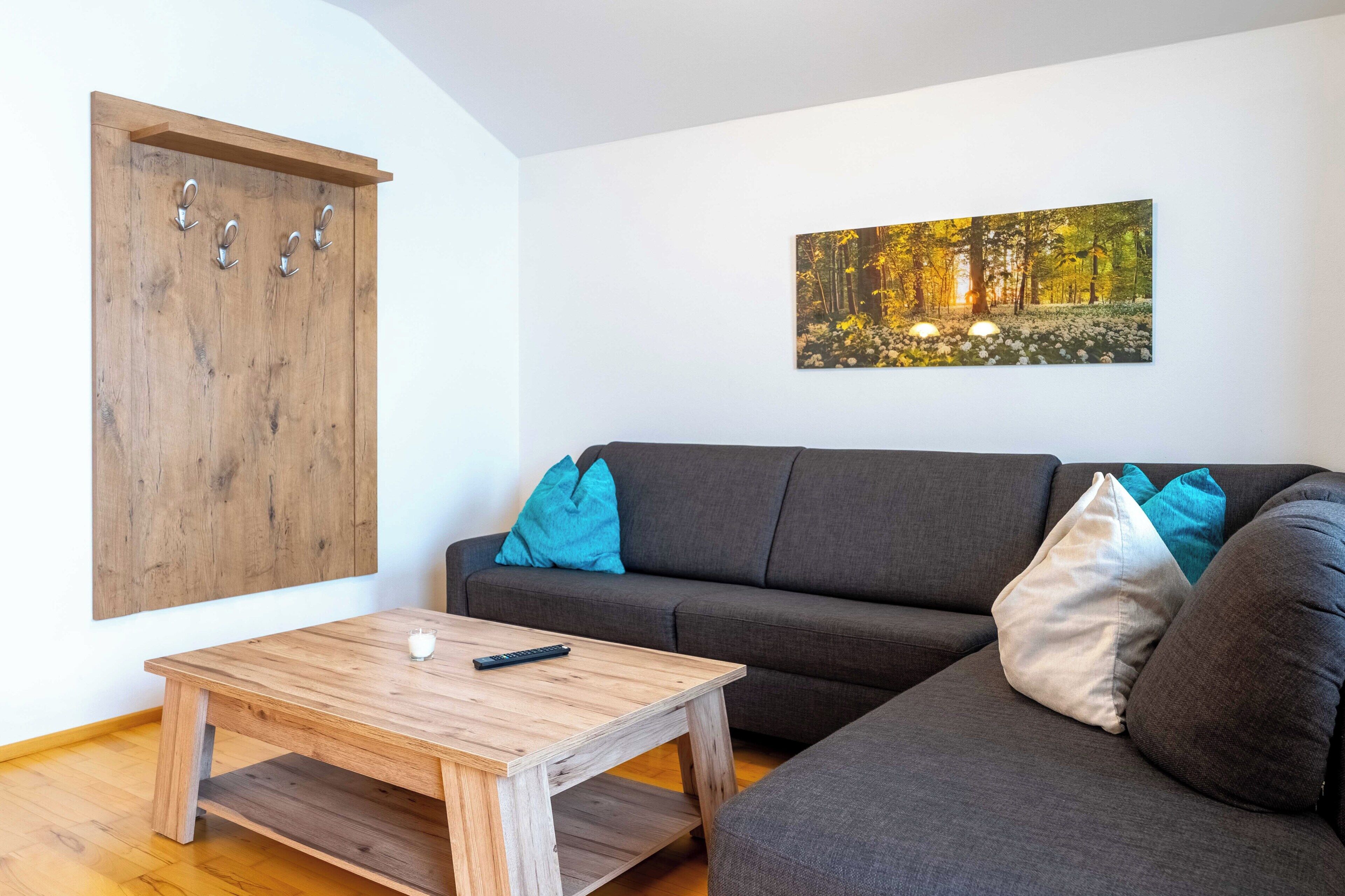 A living room with a wooden table, a grey sofa with blue and white cushions, and a wooden wardrobe with hooks.