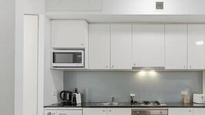 Uma cozinha moderna com armários brancos, micro-ondas, cafeteira, chaleira, pia, fogão e forno.