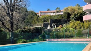 Una piscina blu cristallina circondata da un solarium in pietra, con una recinzione e vegetazione sullo sfondo.