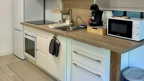 Una cucina compatta con mobili bianchi, un forno a microonde, un bollitore e un cestino.