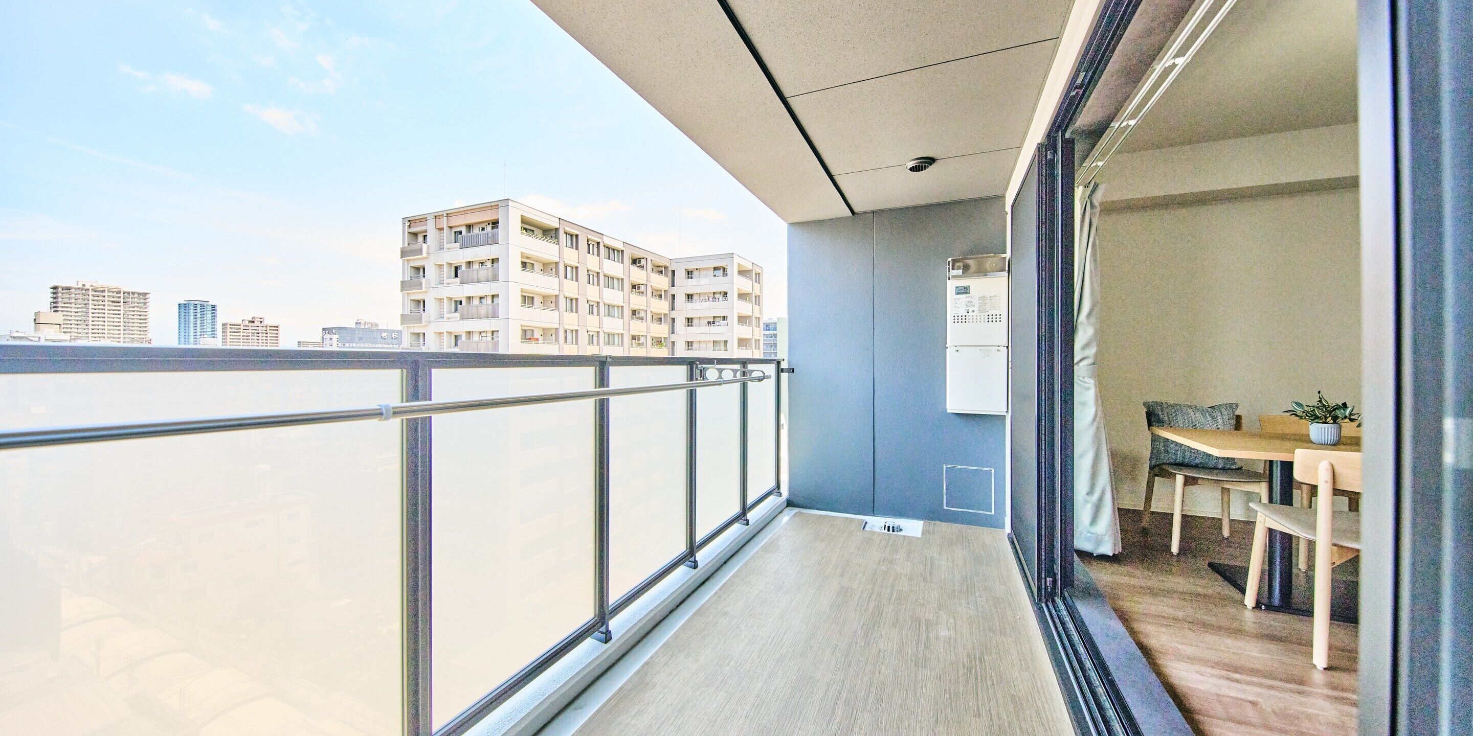 A balcony with a view of a cityscape, a small table with chairs, and a power outlet on the wall.