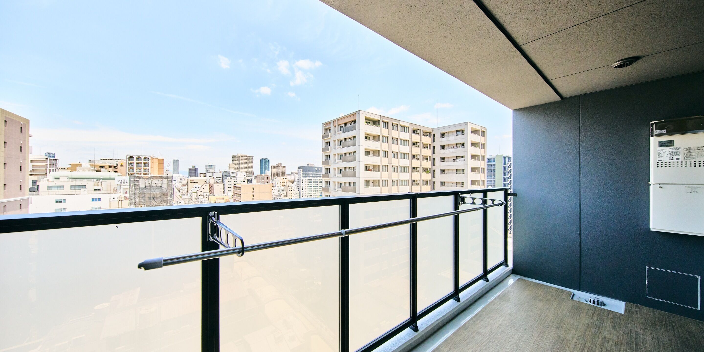 A balcony with a metal railing, a view of a cityscape, and a wall-mounted electrical box.