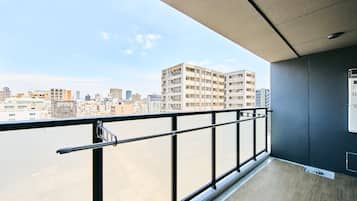 A balcony with a metal railing, a view of a cityscape, and a wall-mounted electrical box.