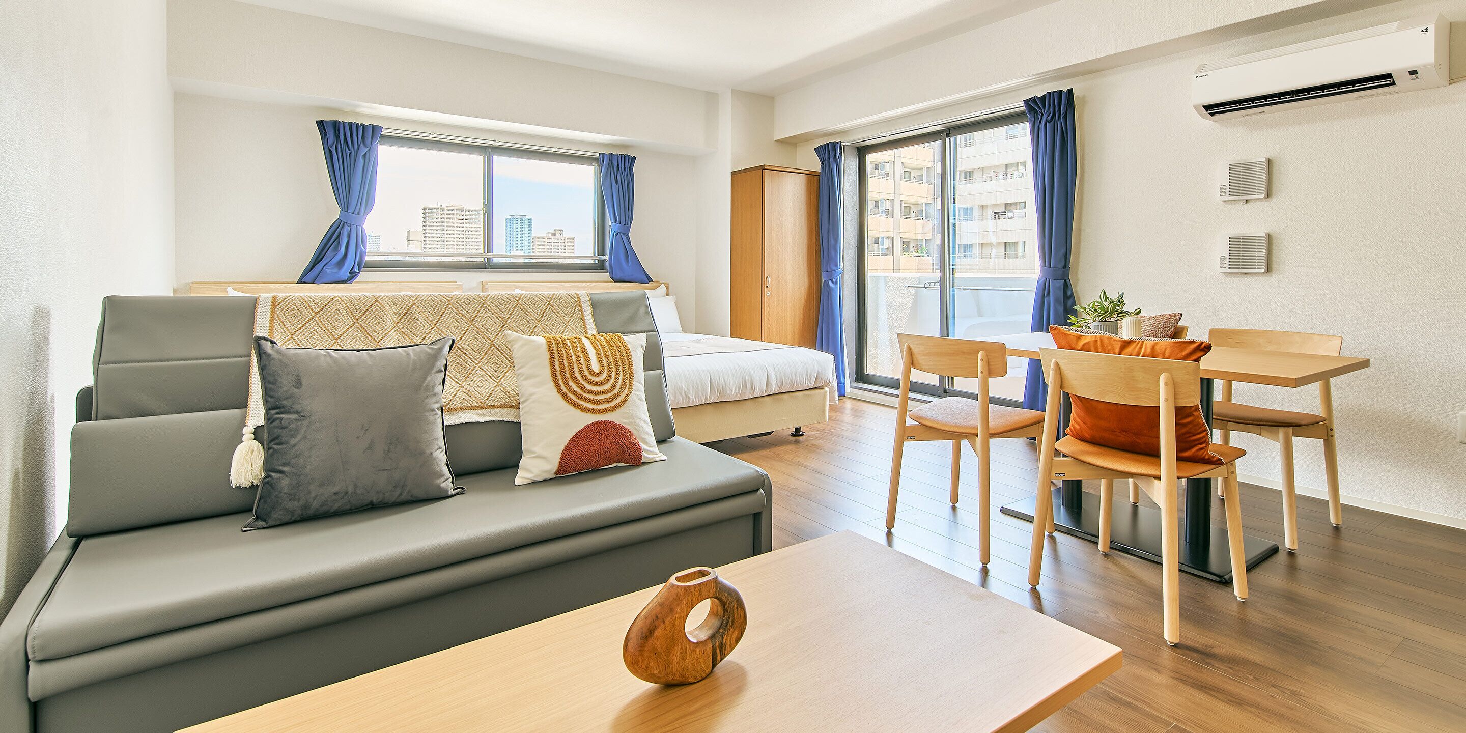 A modern living room with a sofa, a dining table, and a view of the city through large windows.