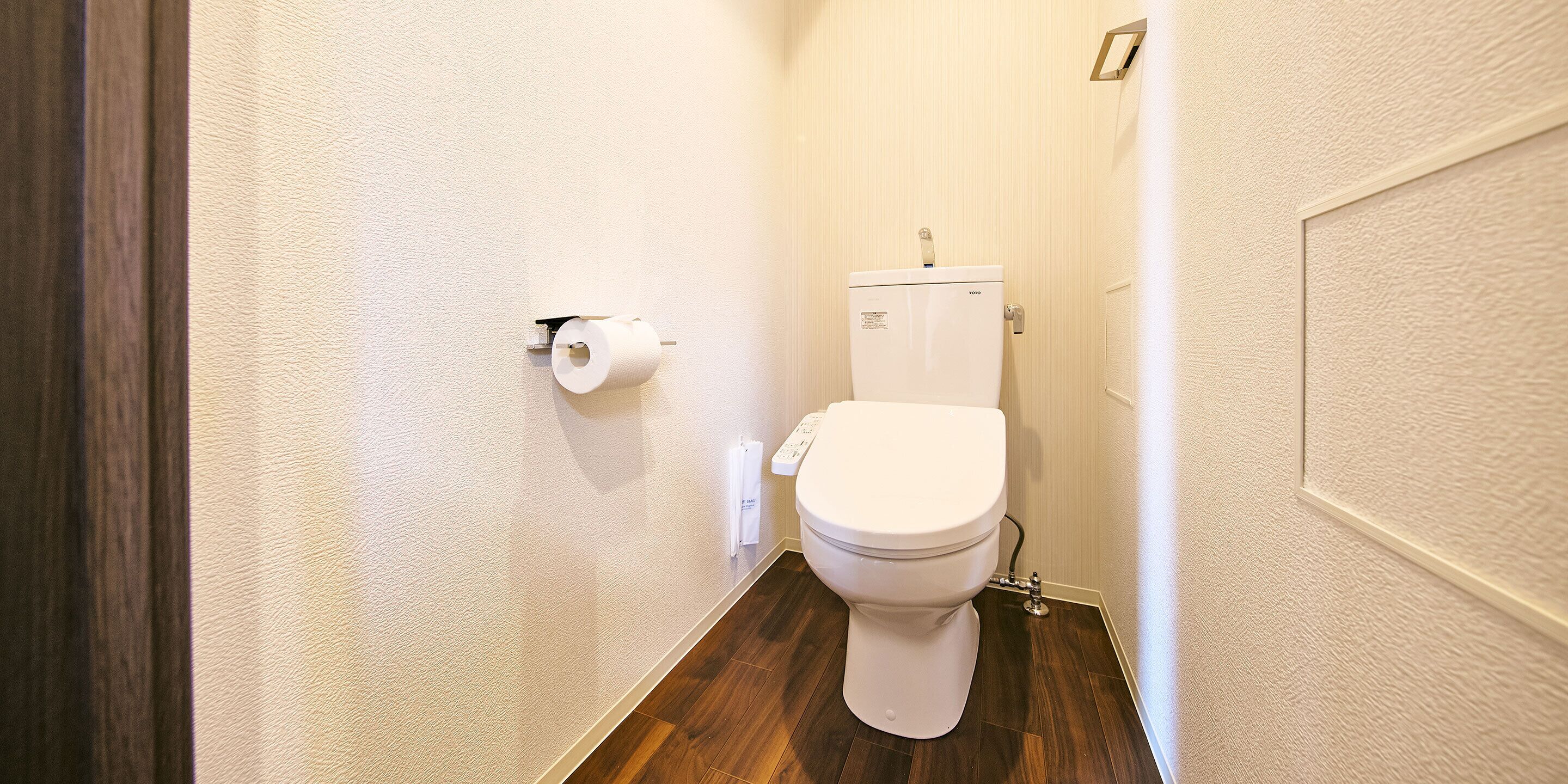 A small bathroom with a toilet, a toilet paper holder, and a white wall.