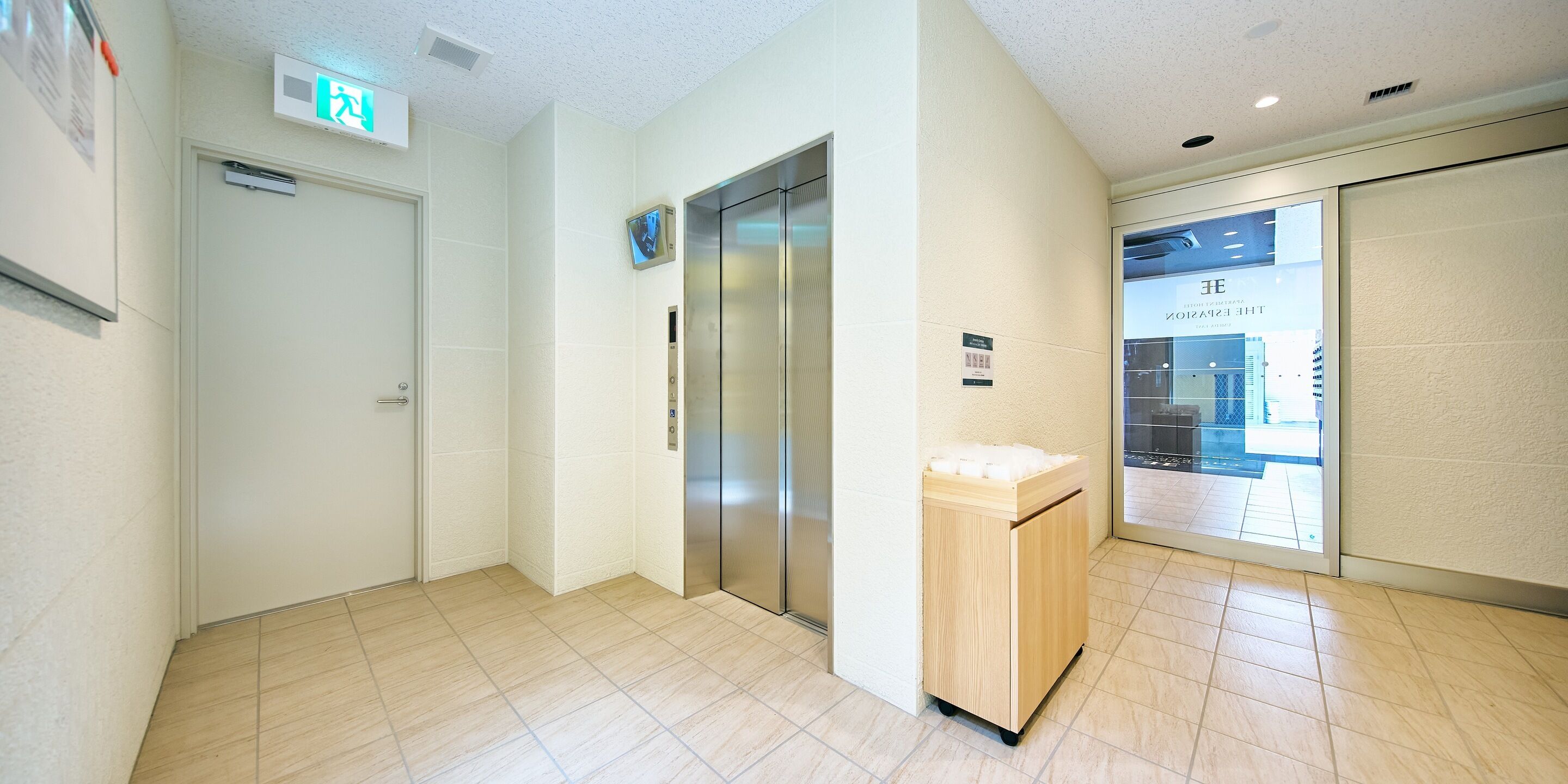 A hotel lobby with an elevator, a reception desk, and a glass door leading to a spa area.