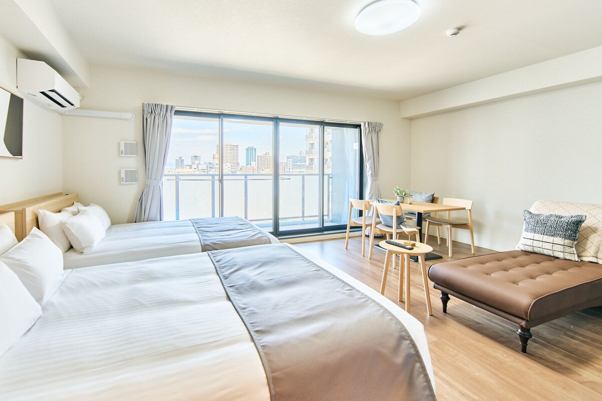 Quarto de hotel com duas camas, uma mesa de jantar, uma cadeira e vista para a cidade.