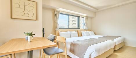 Quarto de hotel com cama, escrivaninha, cadeira, planta em vaso e janela com cortinas.