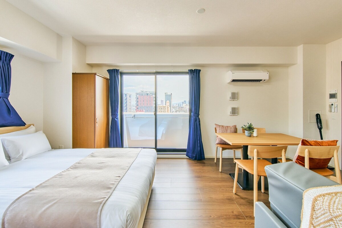 Quarto de hotel com cama, mesa de jantar com cadeiras, varanda com cortinas e ar condicionado.