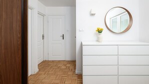 Un couloir avec des portes blanches, un plancher en bois, une commode blanche et un miroir rond accroché au mur.