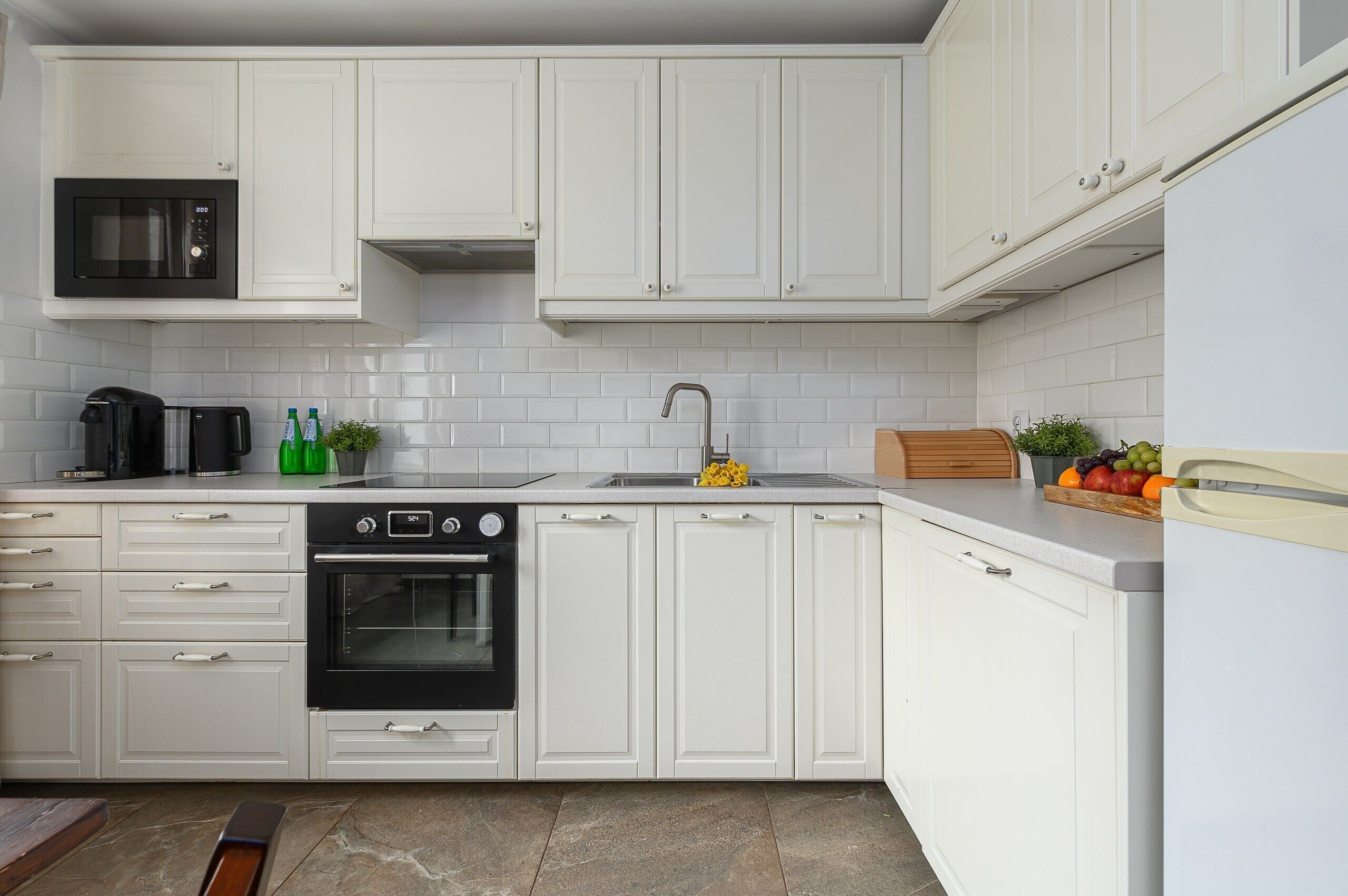 A modern kitchen with white cabinetry, a black oven, a microwave, and a sink.