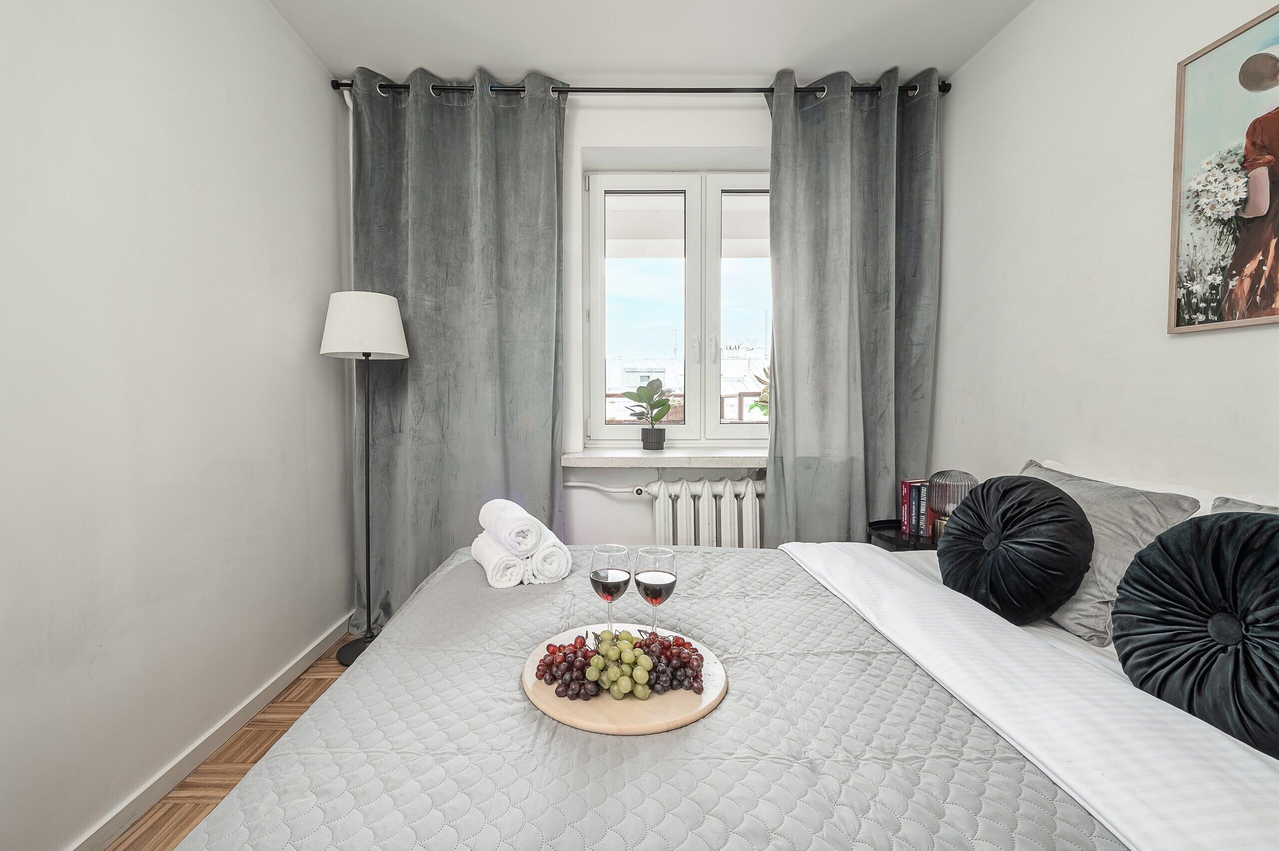 Une chambre à coucher avec un lit, une table de chevet avec une lampe, une fenêtre avec des rideaux, une vue sur le ciel et un tableau accroché au mur.