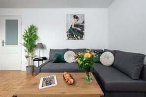 A modern living room with a grey sofa, a coffee table with pastries, a magazine, a potted plant, and a painting on the wall. - Cozy Apartment with balcony near Museum (Warsaw)