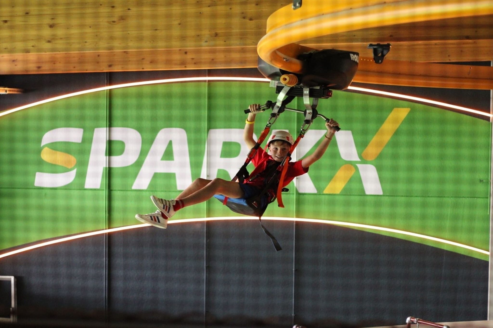 A person bungee jumping with a harness and helmet, with a large 'SPARKX' logo on the background.