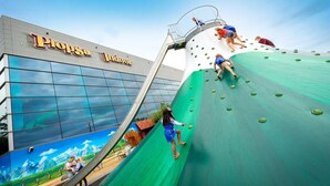 Um edifício com uma placa indicando 'Plopsa Indoor' e uma grande estrutura de escalada com crianças a escalar.