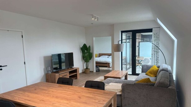 A modern living room with a wooden dining table, grey sofa, and a TV. - Modern apartment Hasselt 2p (Hasselt)