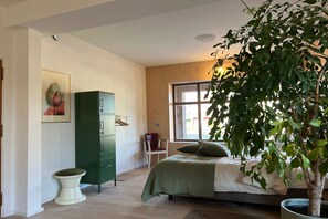 A bedroom with a bed, a green cabinet, a chair, a toilet, and a window with a view.