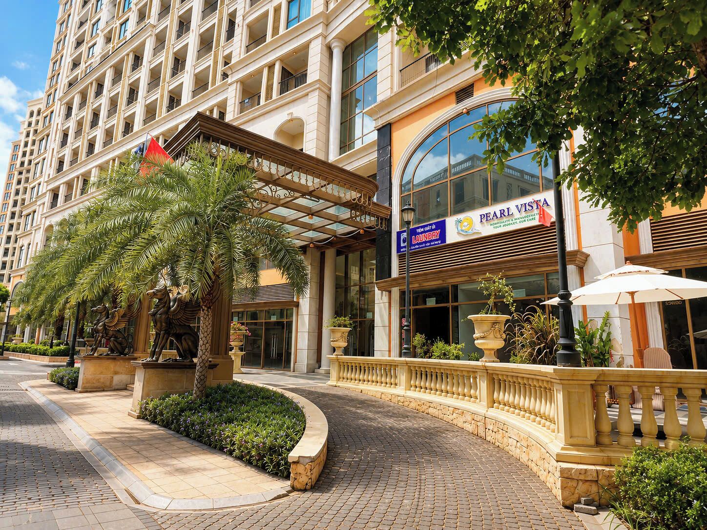 L’entrée d’un hôtel, avec un palmier, une enseigne indiquant « Pearl Vista », et un espace extérieur bien entretenu.