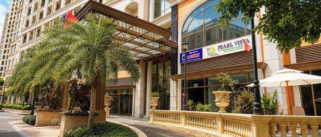 L’entrée d’un hôtel, avec un palmier, une enseigne indiquant « Pearl Vista », et un espace extérieur bien entretenu.