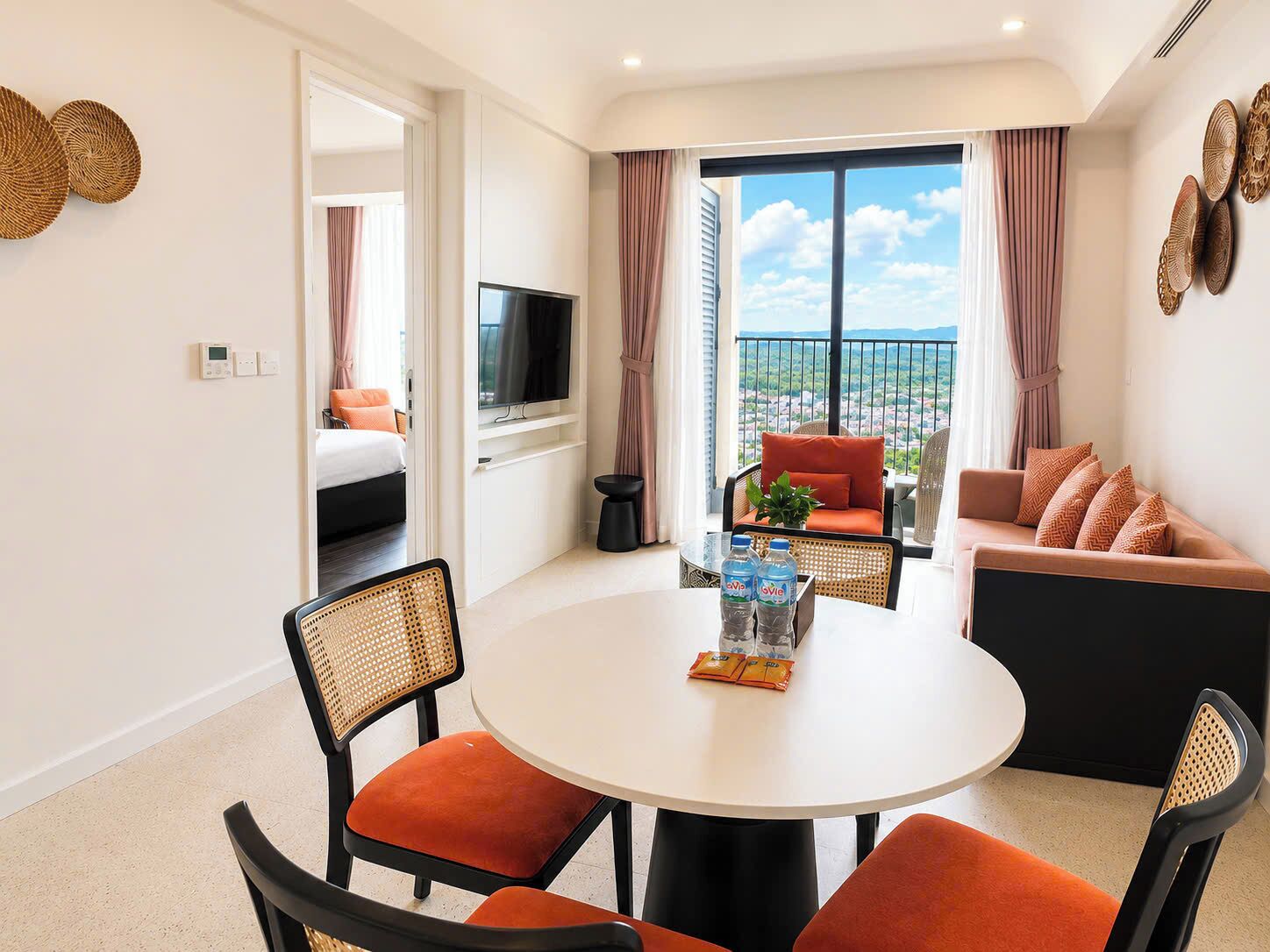 A modern hotel room with a balcony, a round dining table, and a sofa.