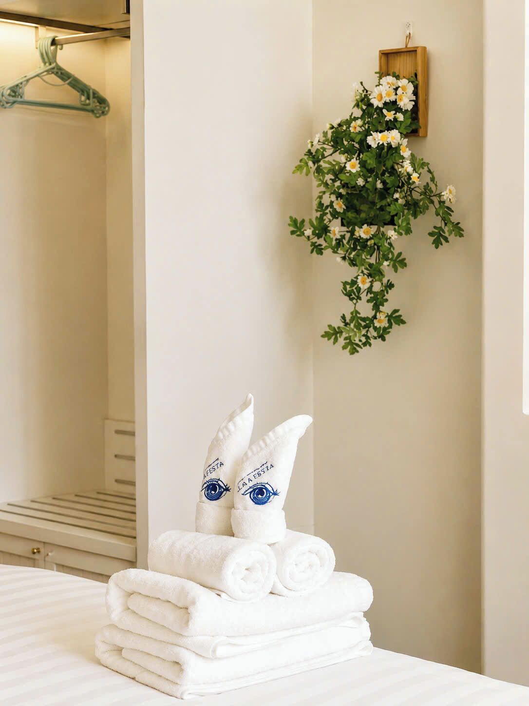 A neatly arranged stack of white towels and a pair of slippers with an eye design on a bed in a hotel room.