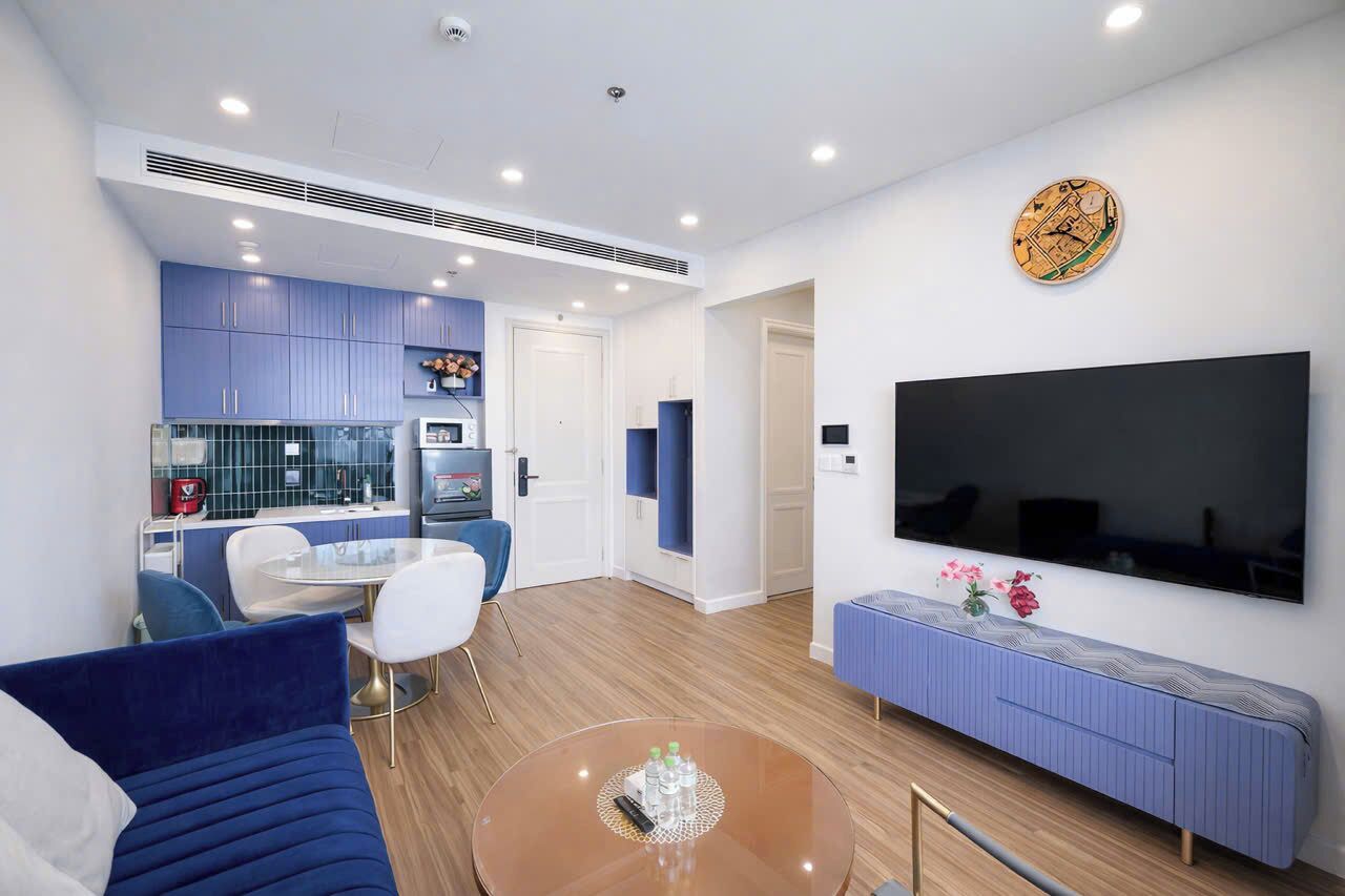 A modern living room with a blue sofa, a round coffee table, and a flat-screen TV mounted on the wall.