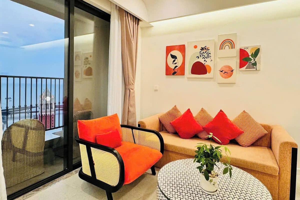 A modern living room with a sofa, armchair, and round coffee table, a balcony with a view, and abstract wall art.