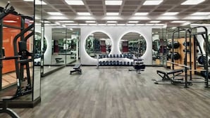 Uma academia com paredes espelhadas, equipamentos de musculação e piso de madeira.
