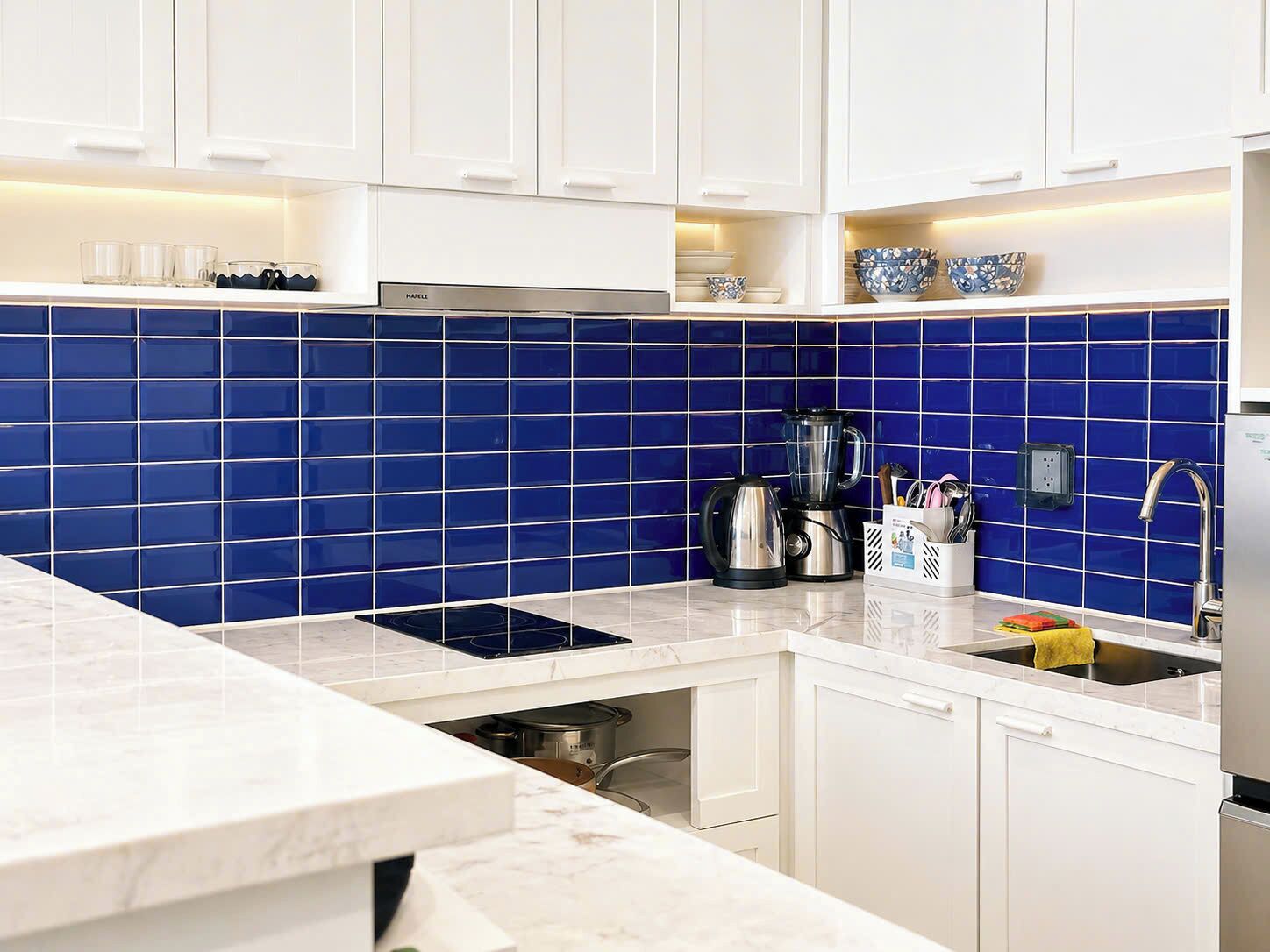 A modern kitchen with white cabinets, a blue tiled backsplash, a built-in stove, and a coffee maker.