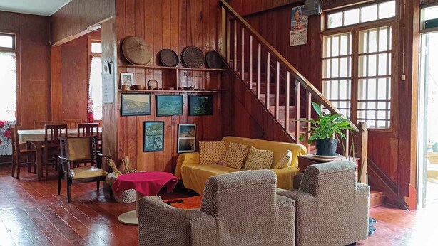 A wooden interior with a staircase, a sofa, a dining table, and a wall with decorative plates.