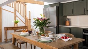 En matplats med ett träbord dukat för frukost, en vas med blommor och ett kök i bakgrunden.