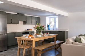 Een moderne keuken met grijze kastjes, een houten eettafel en een bank.