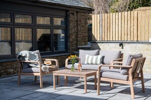Een terras met een houten tafel, twee comfortabele stoelen en een bank.