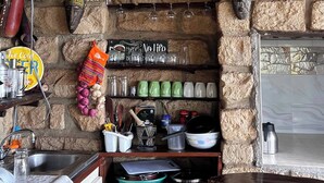 A rustic kitchen with stone walls, wooden beams, a hanging light fixture, and various kitchen utensils and appliances.