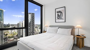 Habitación de hotel con un ventanal grande, una cama, dos mesitas de noche con lámparas y un cuadro en la pared.