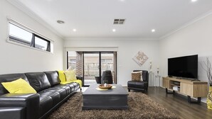 Una sala de estar moderna con un sofá de cuero negro, una mesa de centro, un televisor y un mueble de madera.
