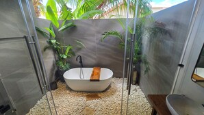 A modern bathroom with a freestanding bathtub, surrounded by pebbles, and featuring glass doors and walls. - Villa Casa Casar in Paje Zanzibar for rent (Sansibar)