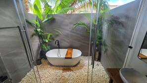 A modern bathroom with a freestanding bathtub, surrounded by pebbles, and featuring glass doors and walls.