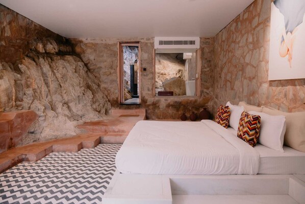 Une chambre avec un mur en pierre, un lit avec une literie blanche et un tapis à motifs.