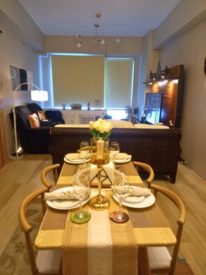 A dining area with a table set for four, a vase with flowers, and a view of a living room in the background. - Exquisite Condo Unit in Eastwood (Quezon City)